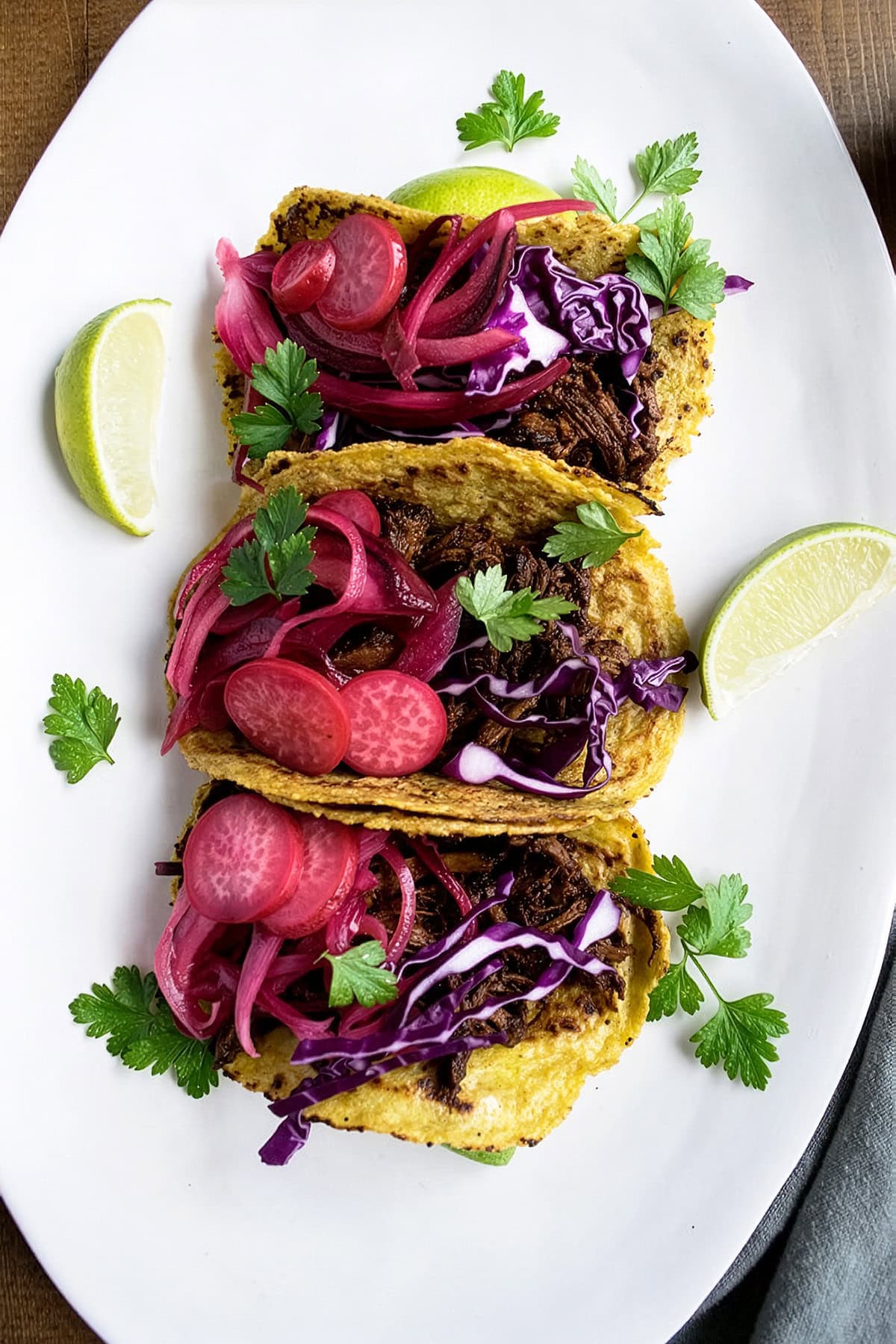 Gluten free Barbacoa brisket tacos topped with red cabbage and pickled radishes and onions on a ceramic serving tray.