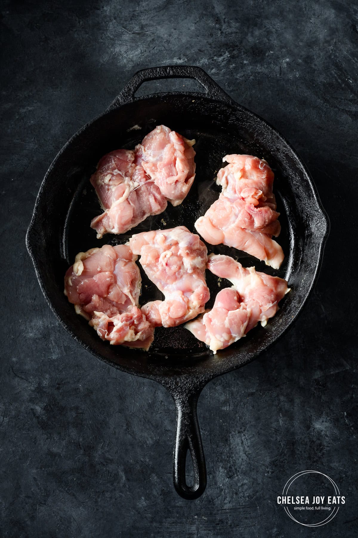 Overhead view of chicken thighs cooking in a cast iron skillet