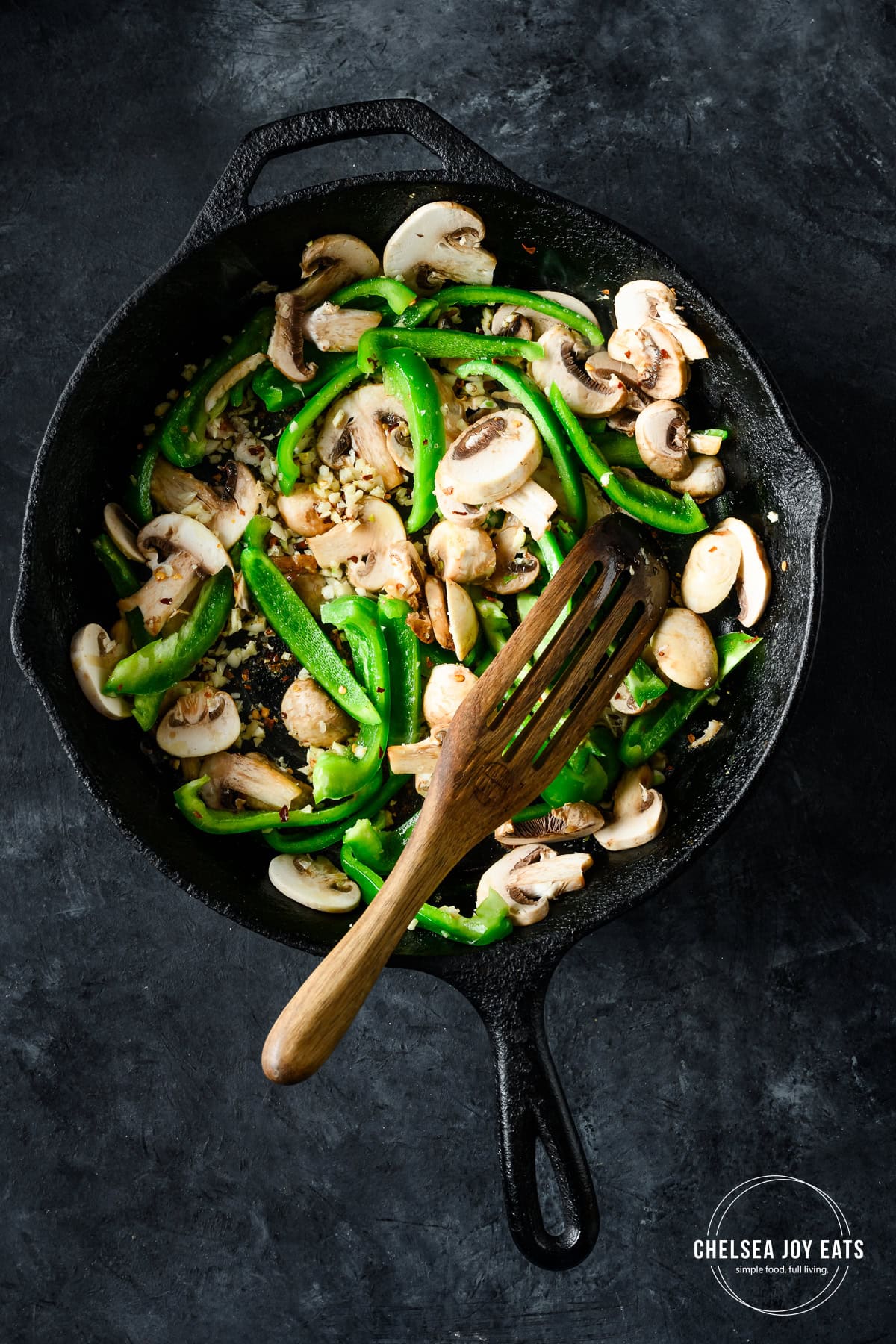 Overhead view of bell peppers, mushrooms, and garlic cooking in a cast iron skillet