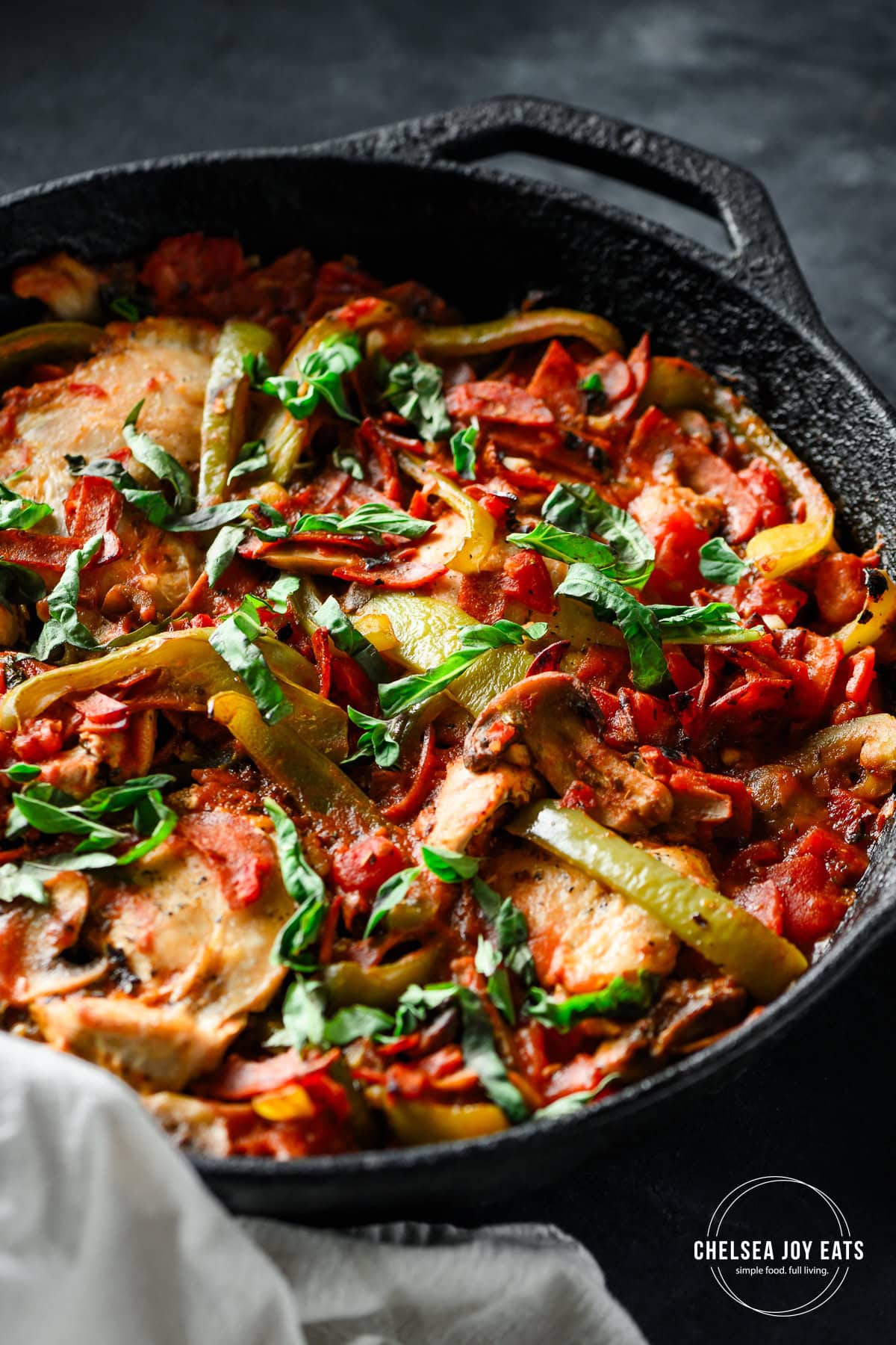 Closeup of a cast iron skillet with a finished pizza chicken casserole with bell peppers and mushrooms