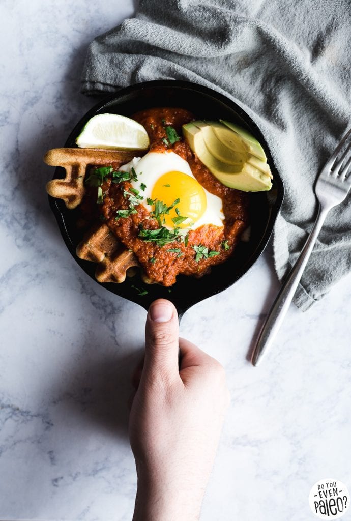 A hand holding a small skillet with gluten free cornbread waffles, homemade salsa, fried egg, lime wedge, and avocado.