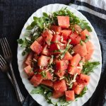 Watermelon Arugula Salad on oval white plate with linen in the background.