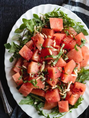 Watermelon Arugula Salad on oval white plate with linen in the background.