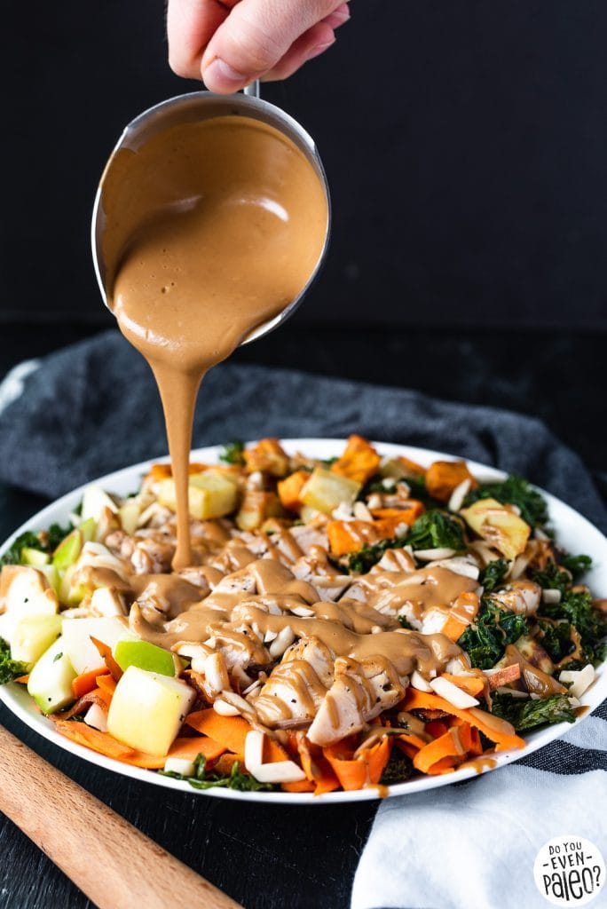 High protein Warm Kale, Chicken, Apple, and Sweet Potato Salad on a white plate with a wooden spoon and dark linens