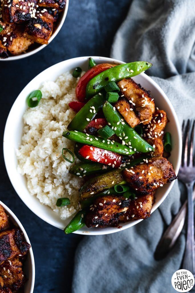 Paleo Pork Belly Stir Fry Recipe with veggies and cauliflower rice in a white bowl on a dark background by DoYouEvenPaleo.net