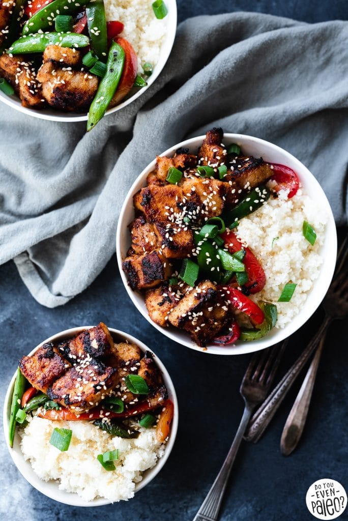 Paleo Pork Belly Stir Fry Recipe with veggies and cauliflower rice arranged in three white bowls on a dark background by DoYouEvenPaleo.net