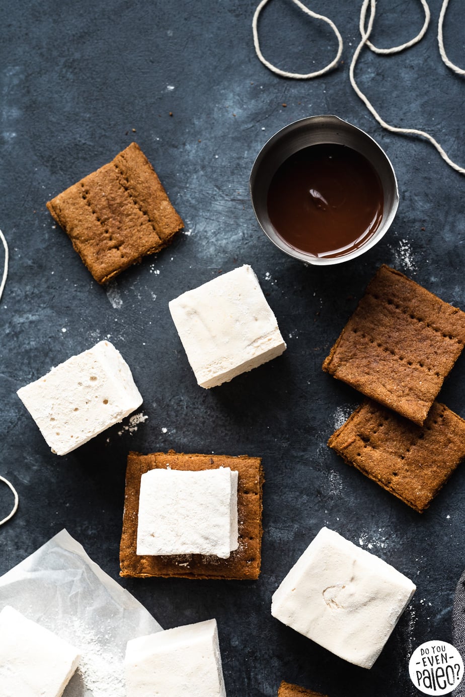 Homemade marshmallows, homemade graham crackers, and a bowl of melted chocolate on a dark background