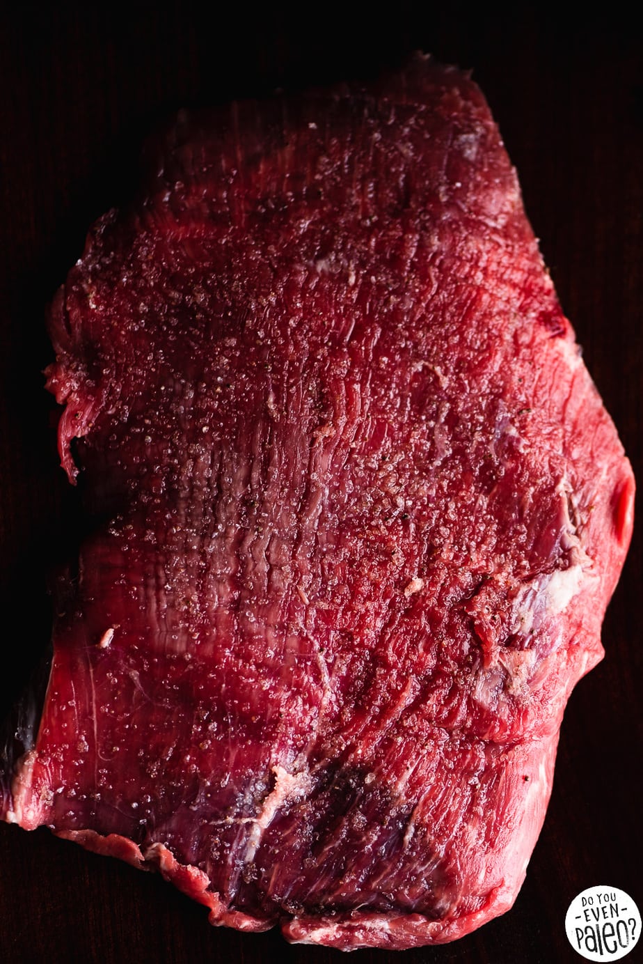 Seasoned raw flank steak on a dark background