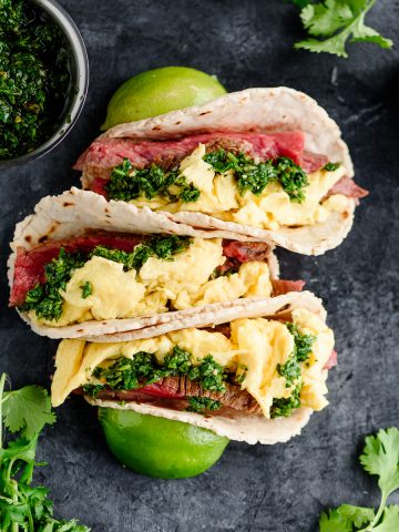 Overhead view of three steak and egg breakfast tacos garnished with chimichurri sauce