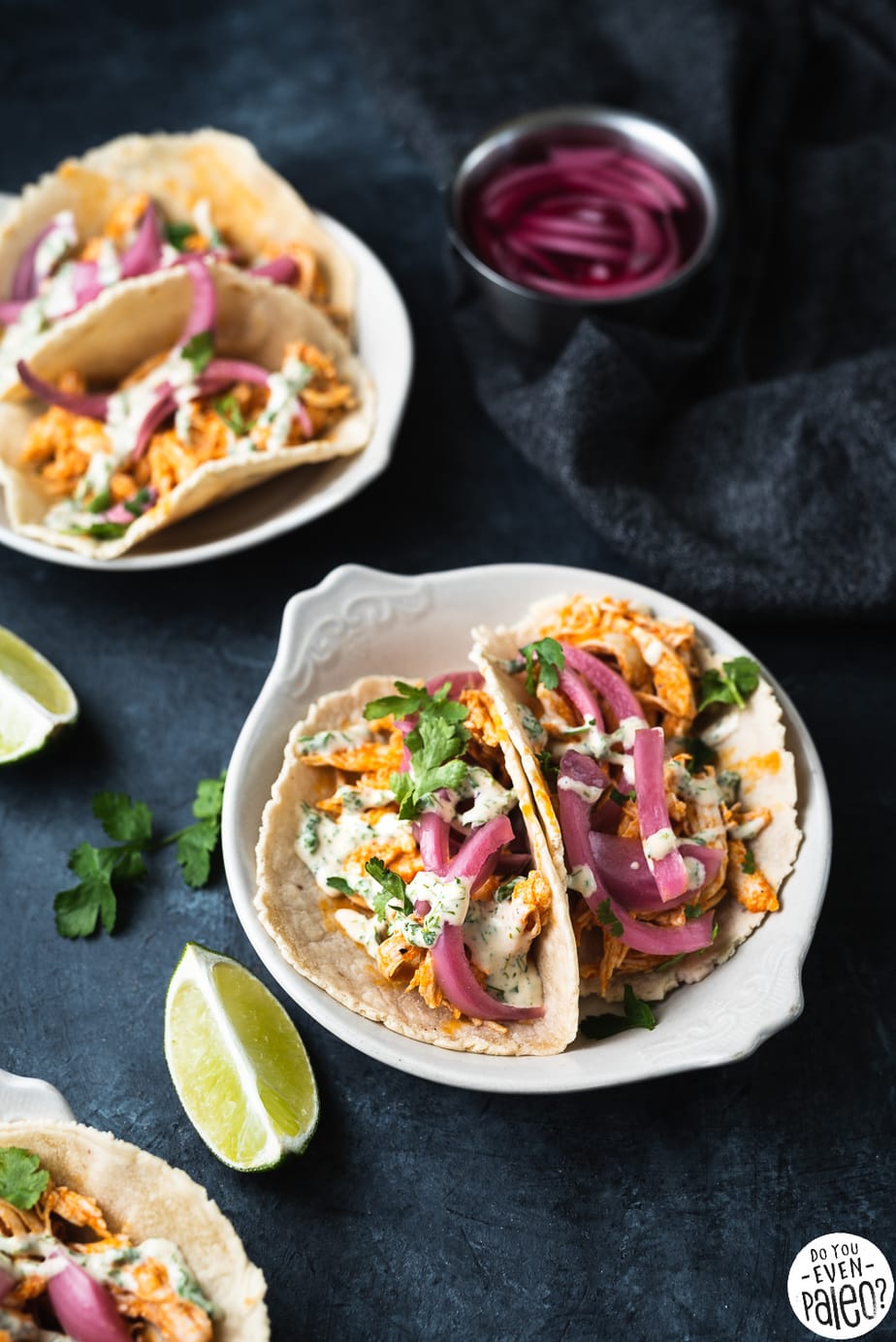 Small plates with buffalo chicken tacos garnished with cilantro, ranch, and pickled onions