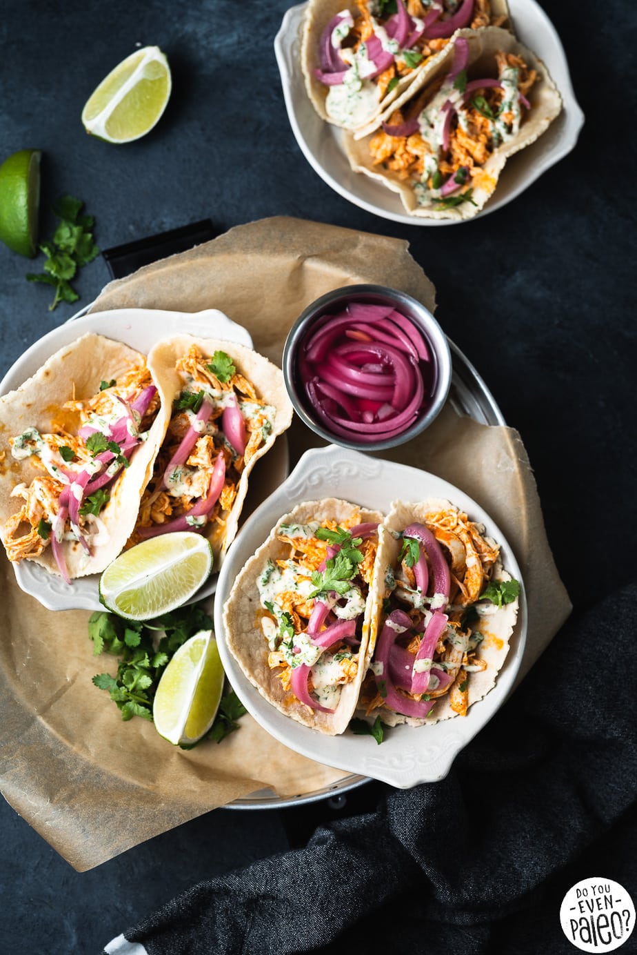 Tacos in small plates on a tray served with pickled red onions and sliced limes