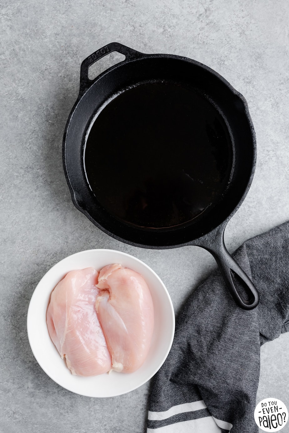 A large deep-bottomed skillet and a bowl with two uncooked chicken breasts