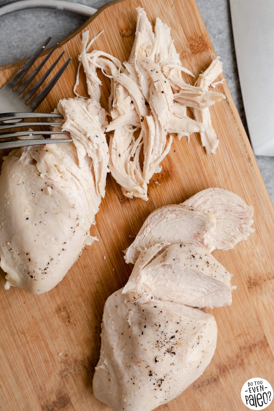 Closeup of chicken breasts being shredded and sliced on a cutting board