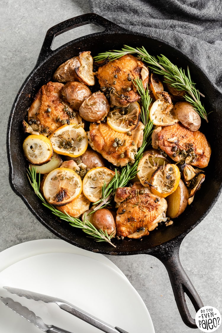 Large cast iron skillet full of chicken thighs, lemon slices, and potatoes