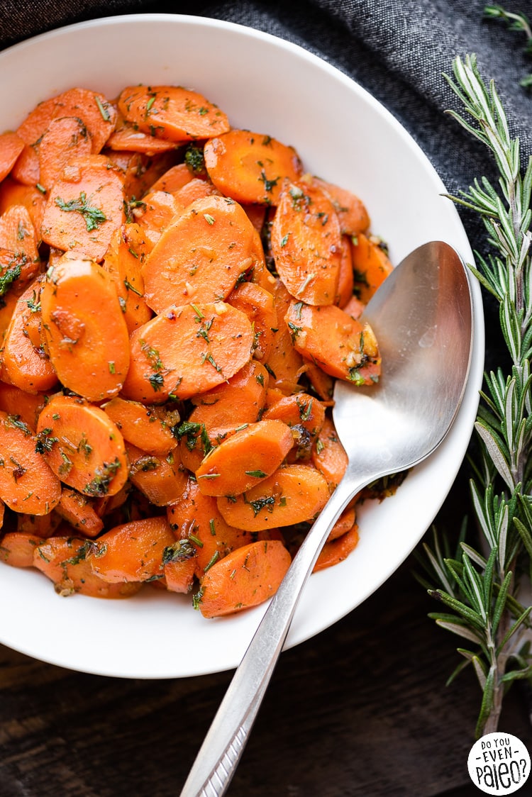 Bowl of herbed garlic carrots with a serving spoon