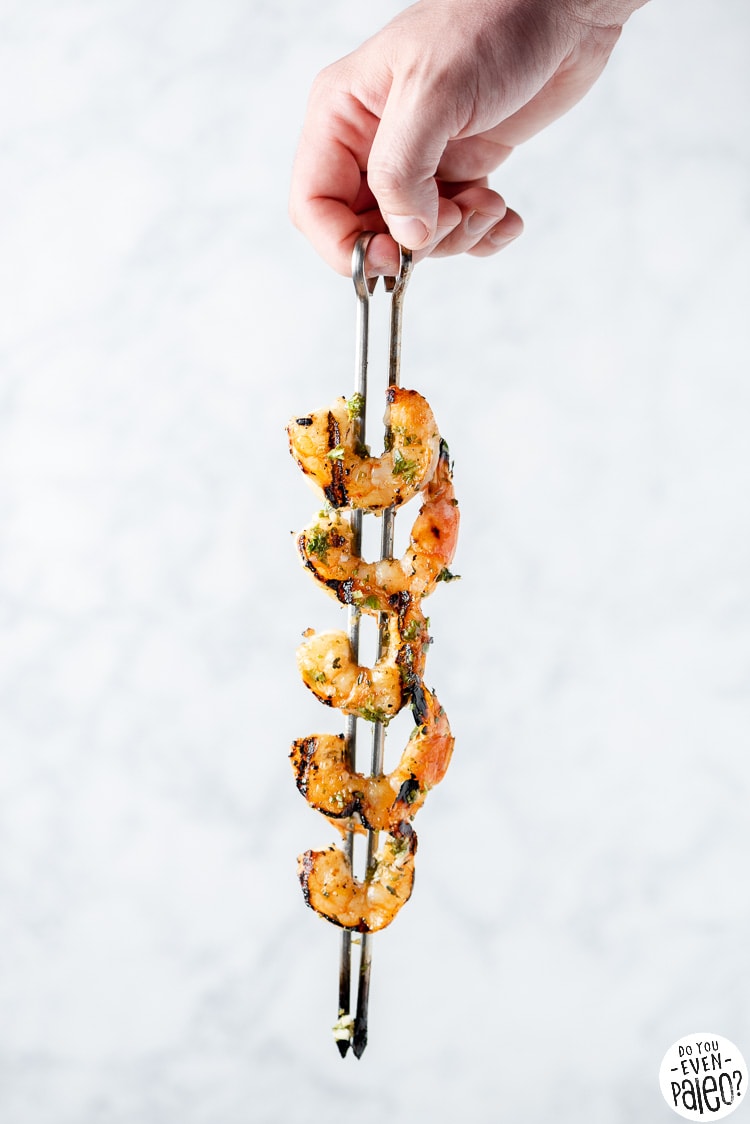 Person holding a skewer of grilled shrimp