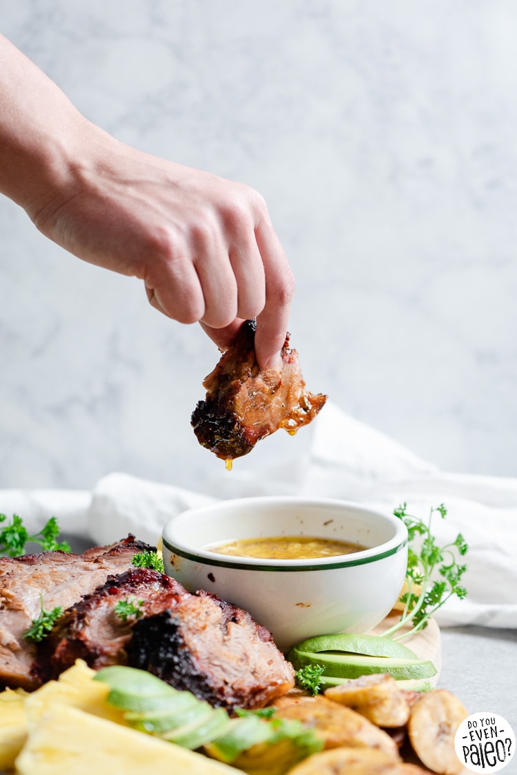 Person dipping smoked pork into a dish of mojo sauce