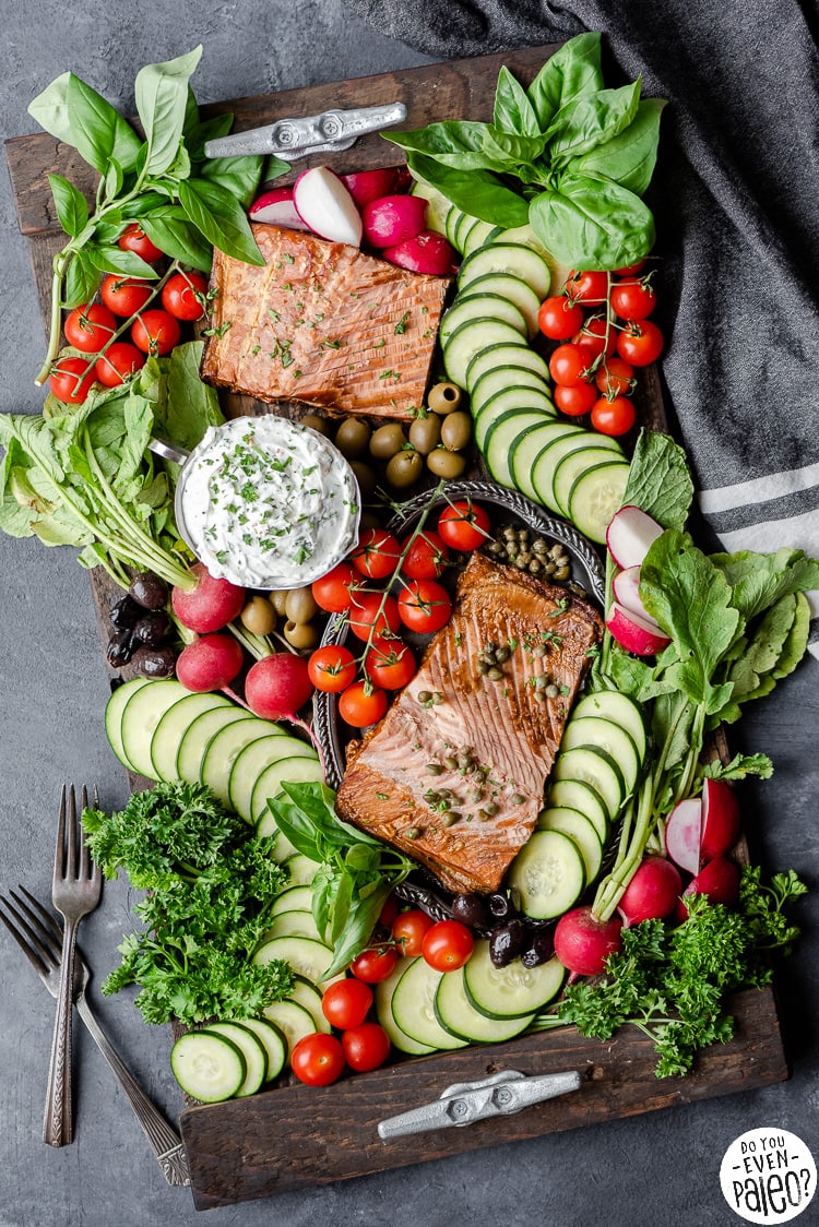 Overhead view of a charcuterie board with smoked salmon, cucumbers, radishes, tomatoes, and herbs