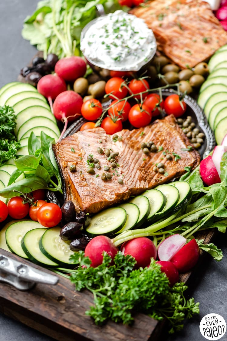 Smoked salmon grazing board with smoked salmon, tomatoes, cucumbers, radishes, and herbs