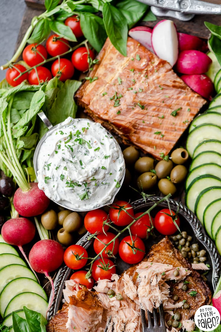 Dish of herbed whipped goat cheese dip on a grazing board with veggies and smoked salmon