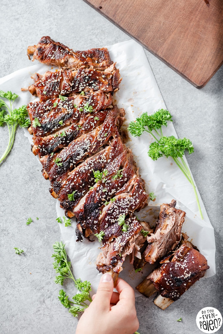 Person picking up a rib from a rack of grilled pork ribs