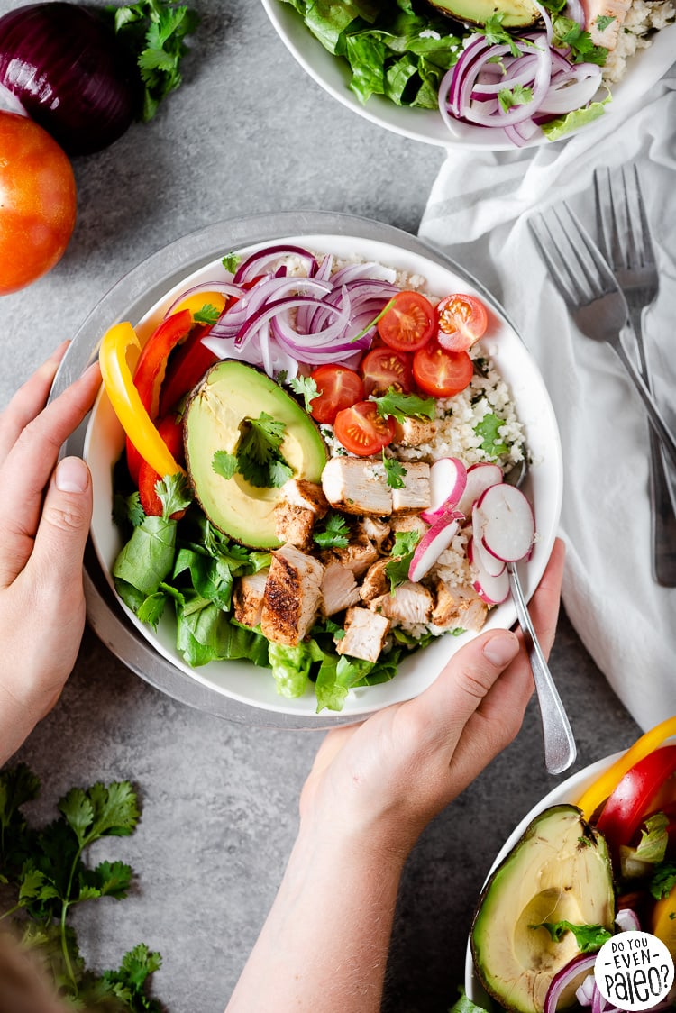 Hands holding a chicken burrito bowl with fresh produce and grilled chicken
