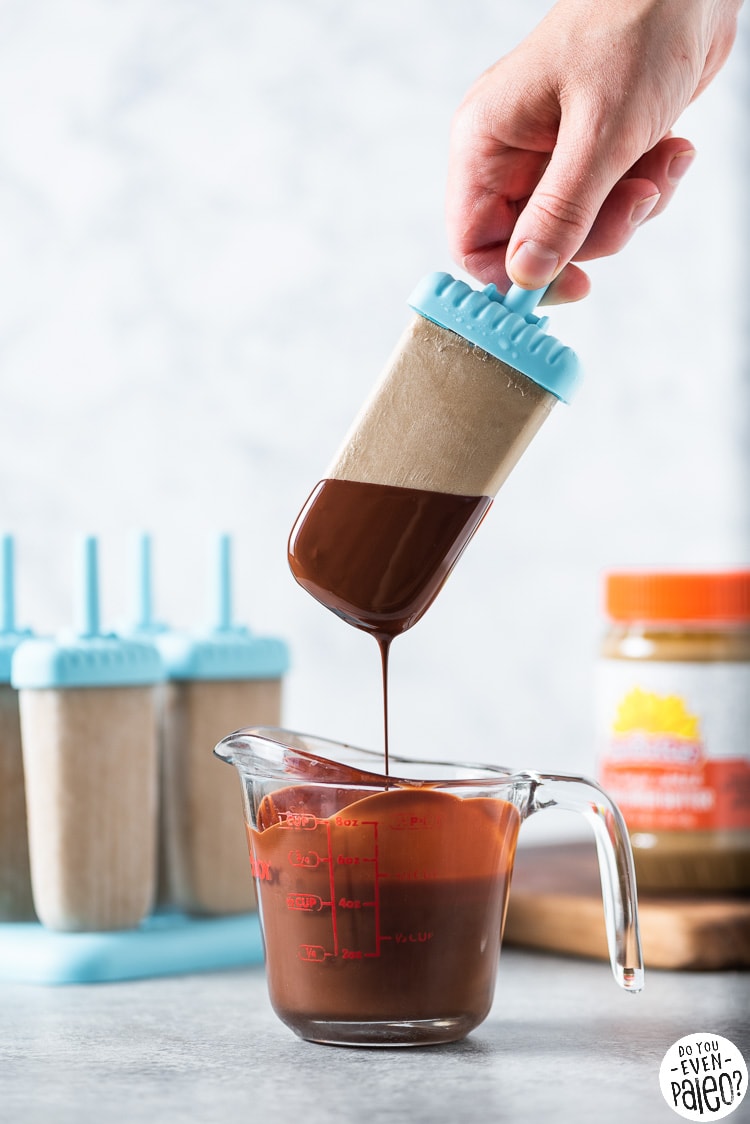 Person dipping a sugar free banana popsicle with peanut butter in melted chocolate
