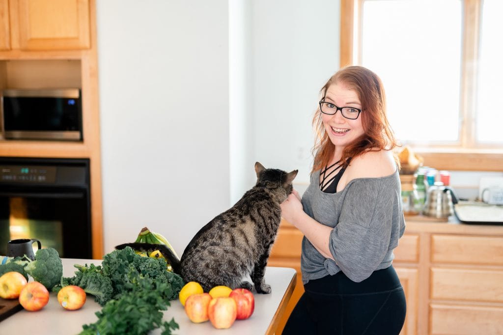 Woman smiling at the camera while petting a cat on a kitchen counter
