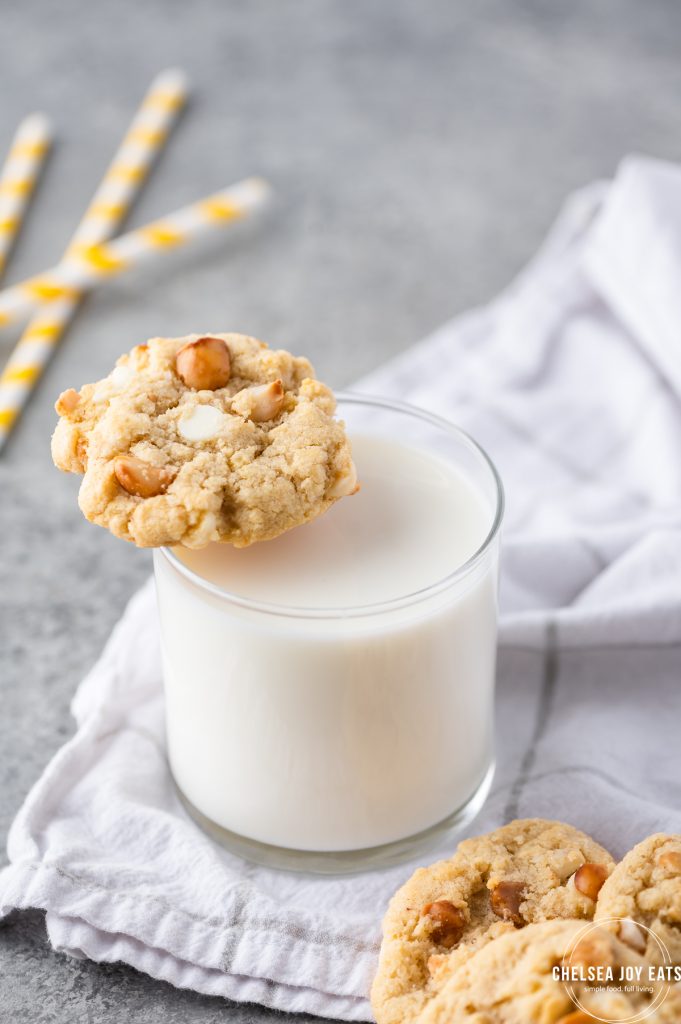 Closeup of a white chocolate macadamia nut cookie balanced on a glass of milk.