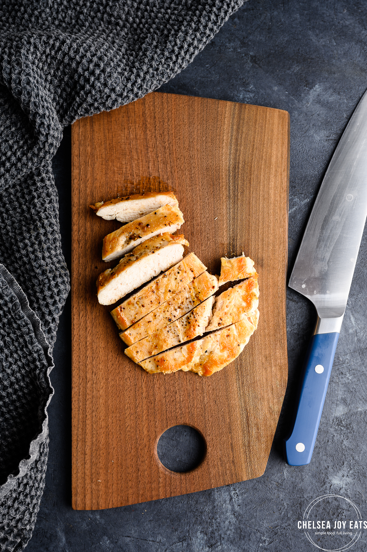 Sliced chicken breast on a cutting board next to a chef's knife