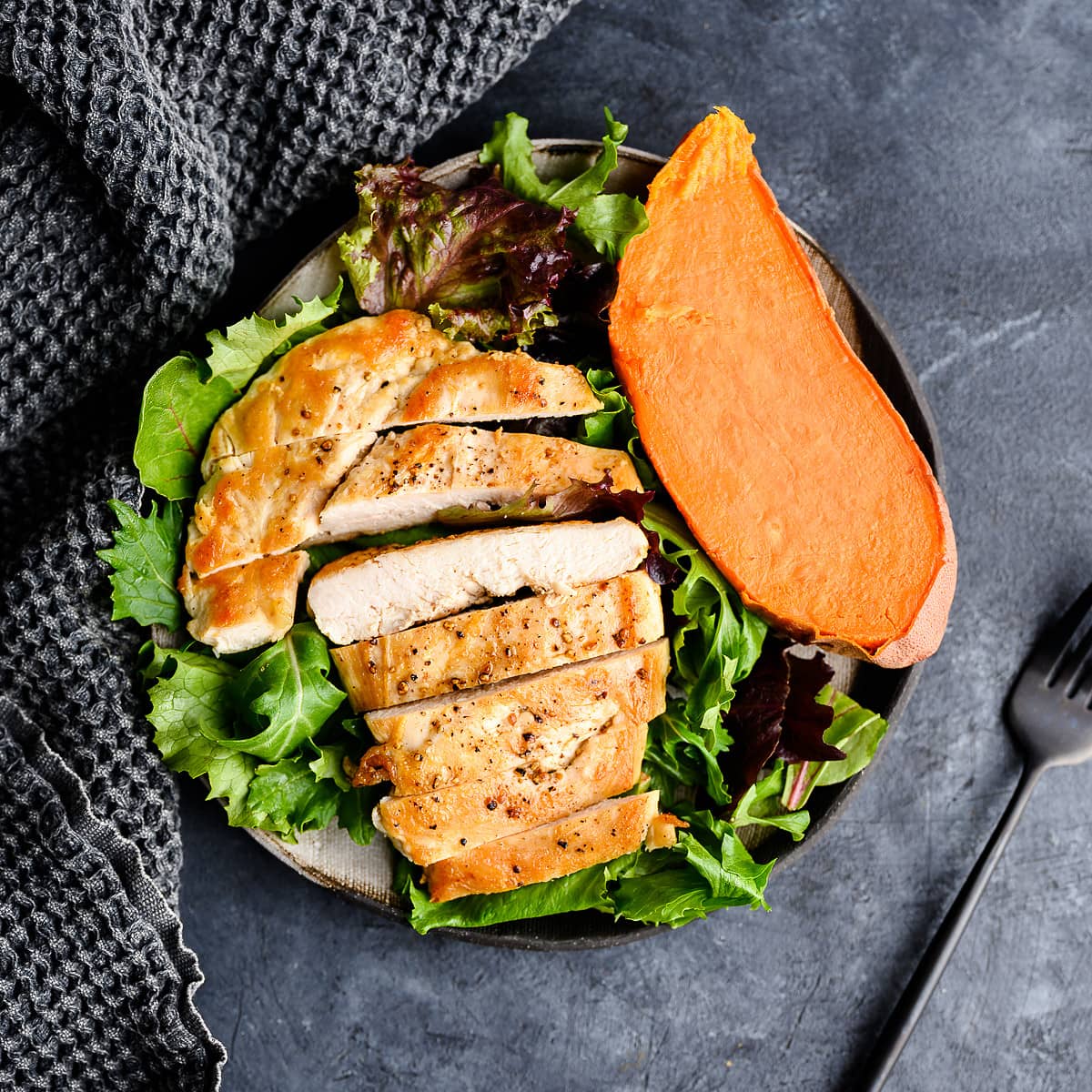 Sliced chicken breast on a bed of lettuce and half a sweet potato