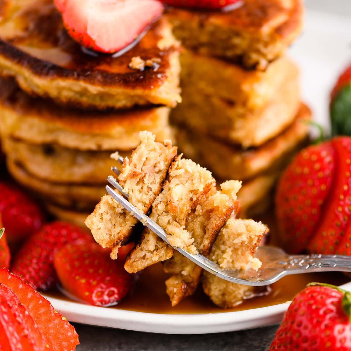 Closeup of a fork loaded with strawberry pancakes, with the stack of pancakes in the background