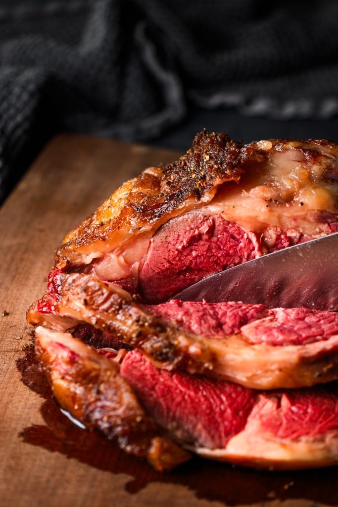 Closeup of a knife slicing a medium reverse sear prime rib roast