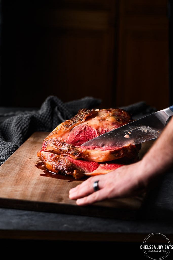 Person slicing a prime rib roast on a wooden cutting board
