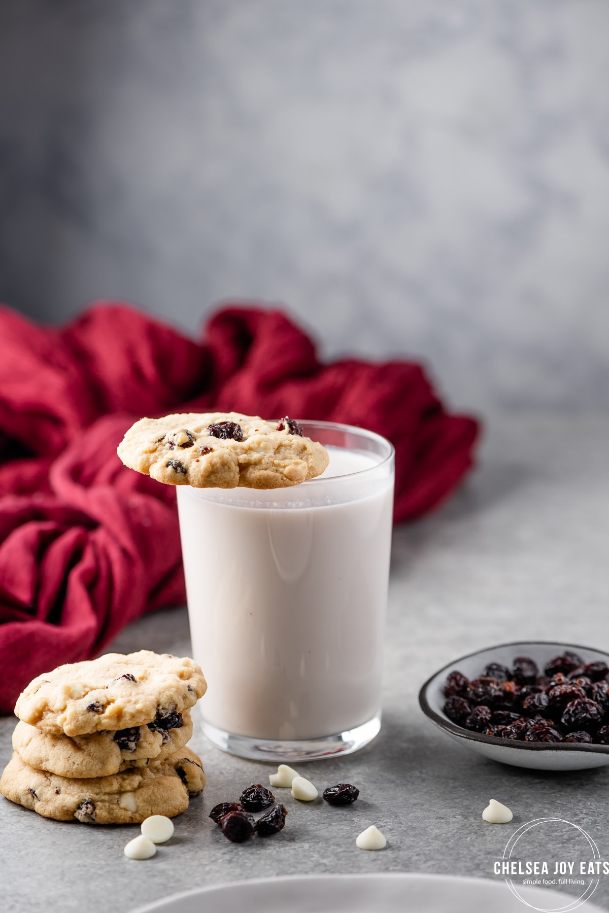 Glass of milk with a Gluten free white chocolate cranberry cookie balanced on the rim