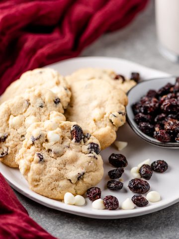 Gluten free white chocolate cranberry cookies arranged on a plate with dried cranberries and white chocolate chips