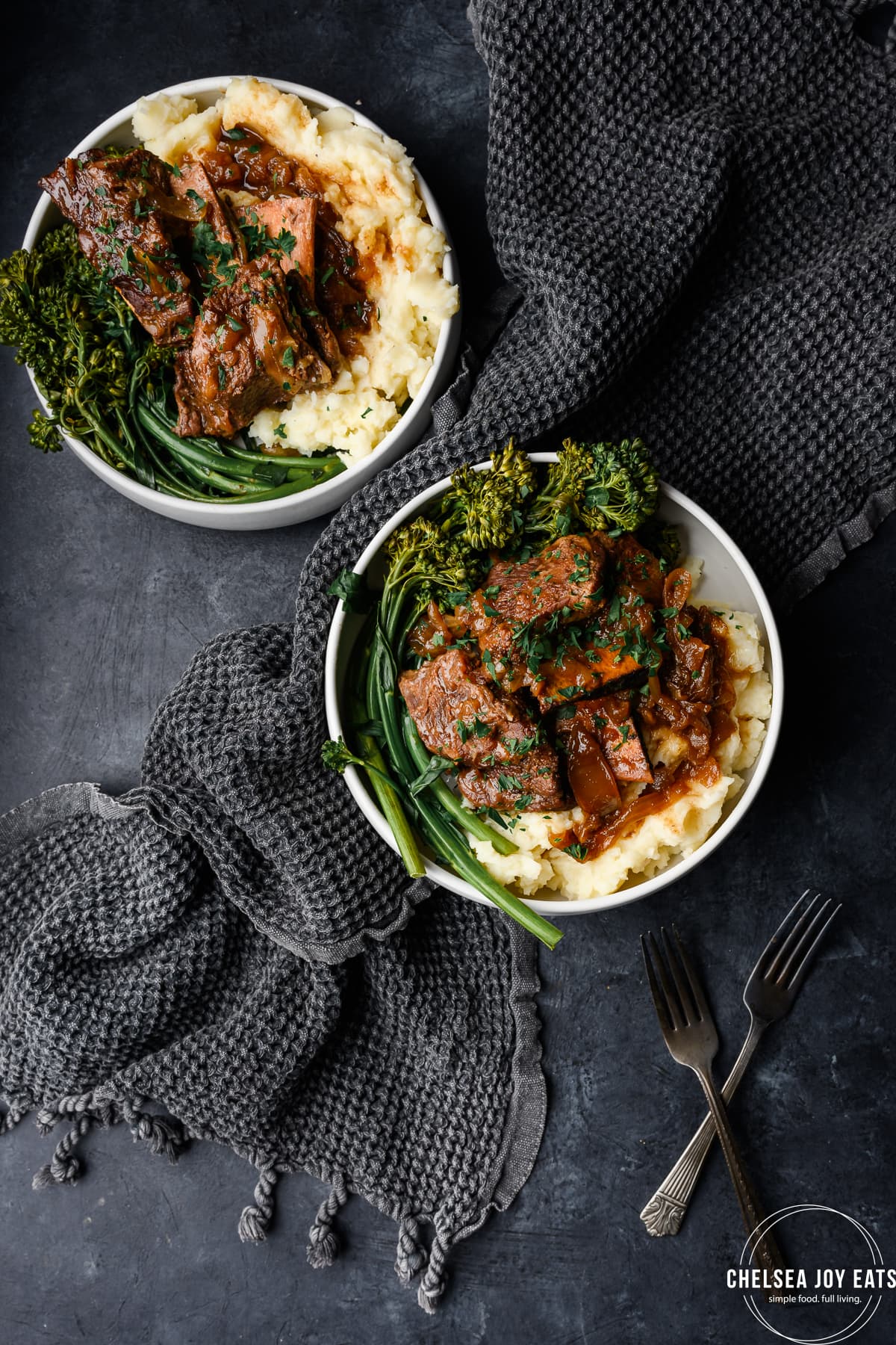 Bird's eye view of cider-braised short ribs in bowls with mashed potatoes and roasted broccolini