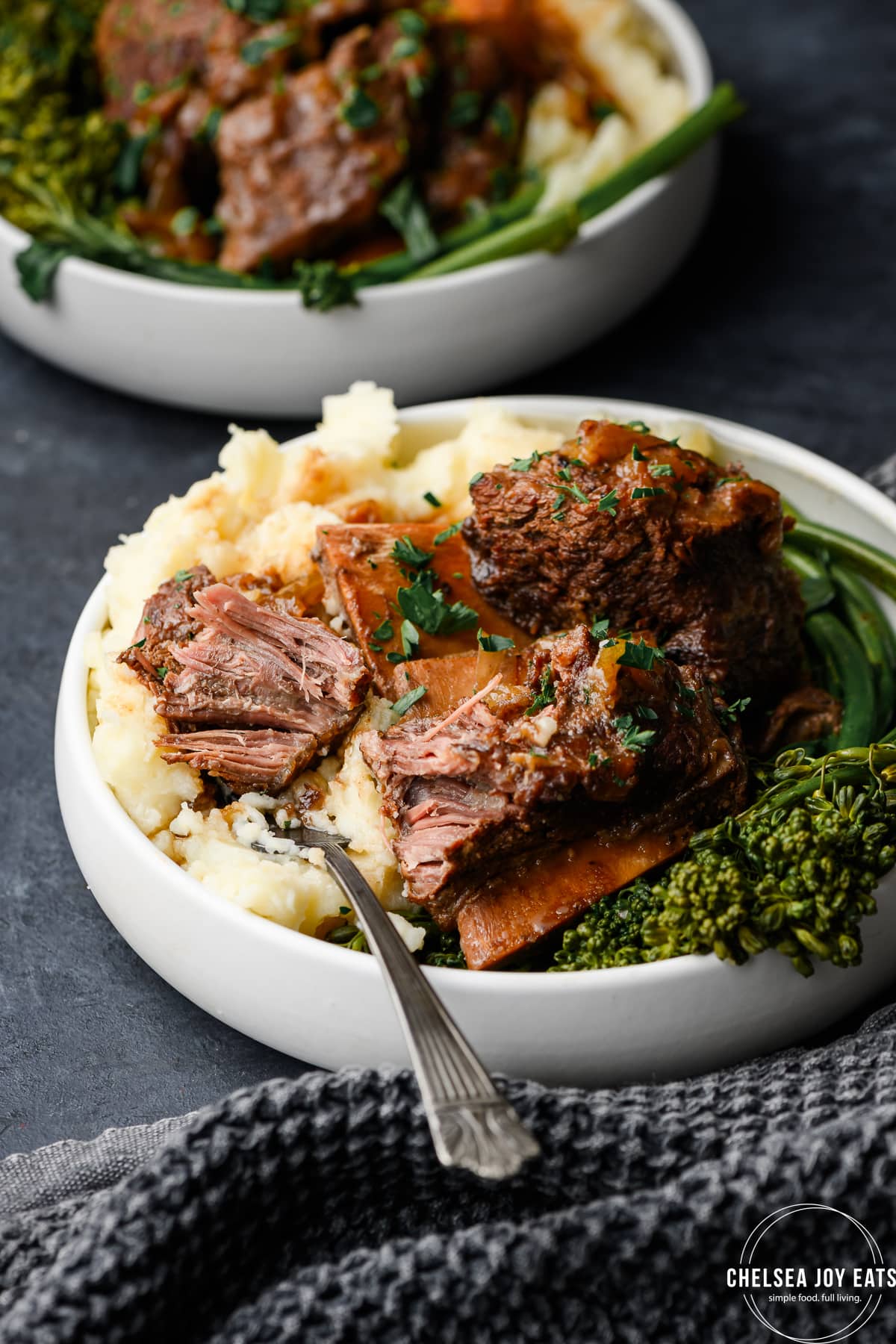 Apple cider braised short ribs over mashed potatoes and roasted broccolini on a dark background