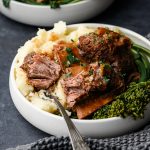 Closeup of cider-braised short ribs over a bed of brocollini and mashed potatoes