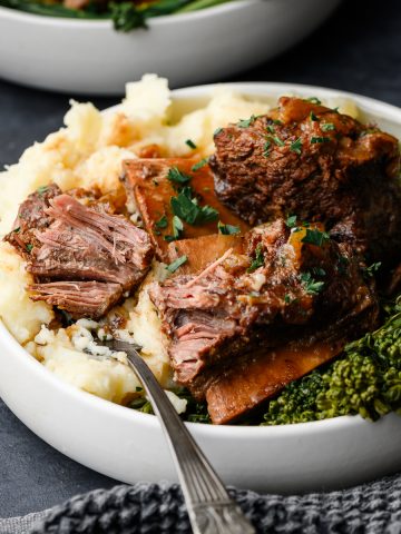 Closeup of cider-braised short ribs over a bed of brocollini and mashed potatoes