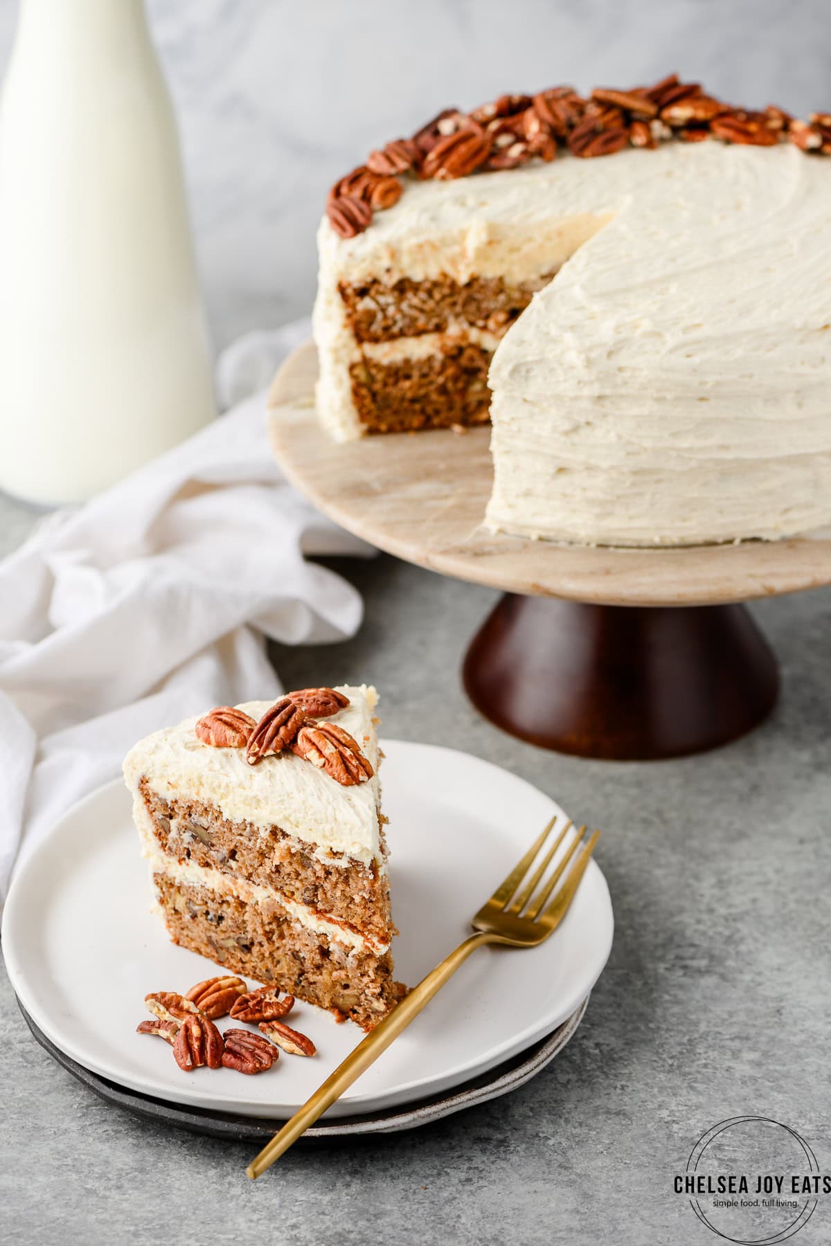 Slice of gluten free hummingbird cake served on a white plate with the full cake in the background