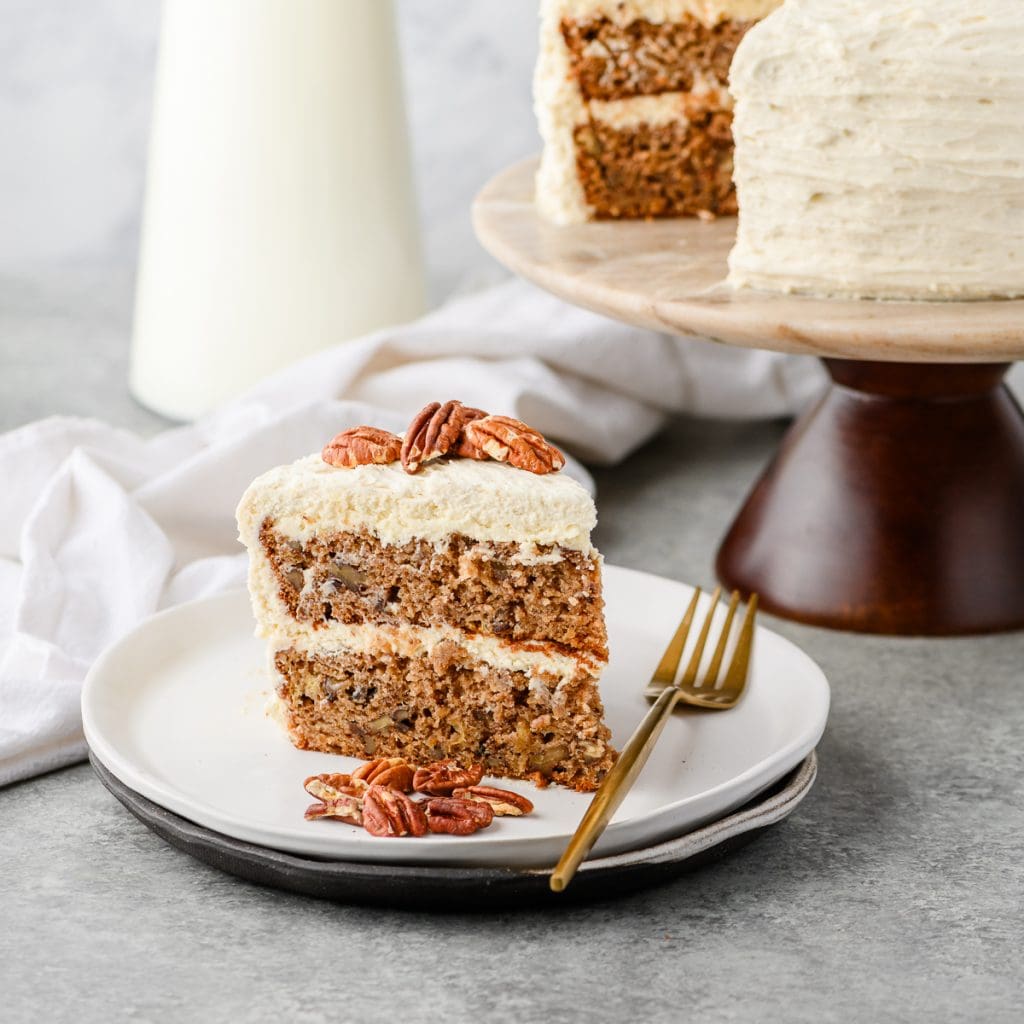 Slice of gluten free hummingbird cake served on a white plate and garnished with pecans.