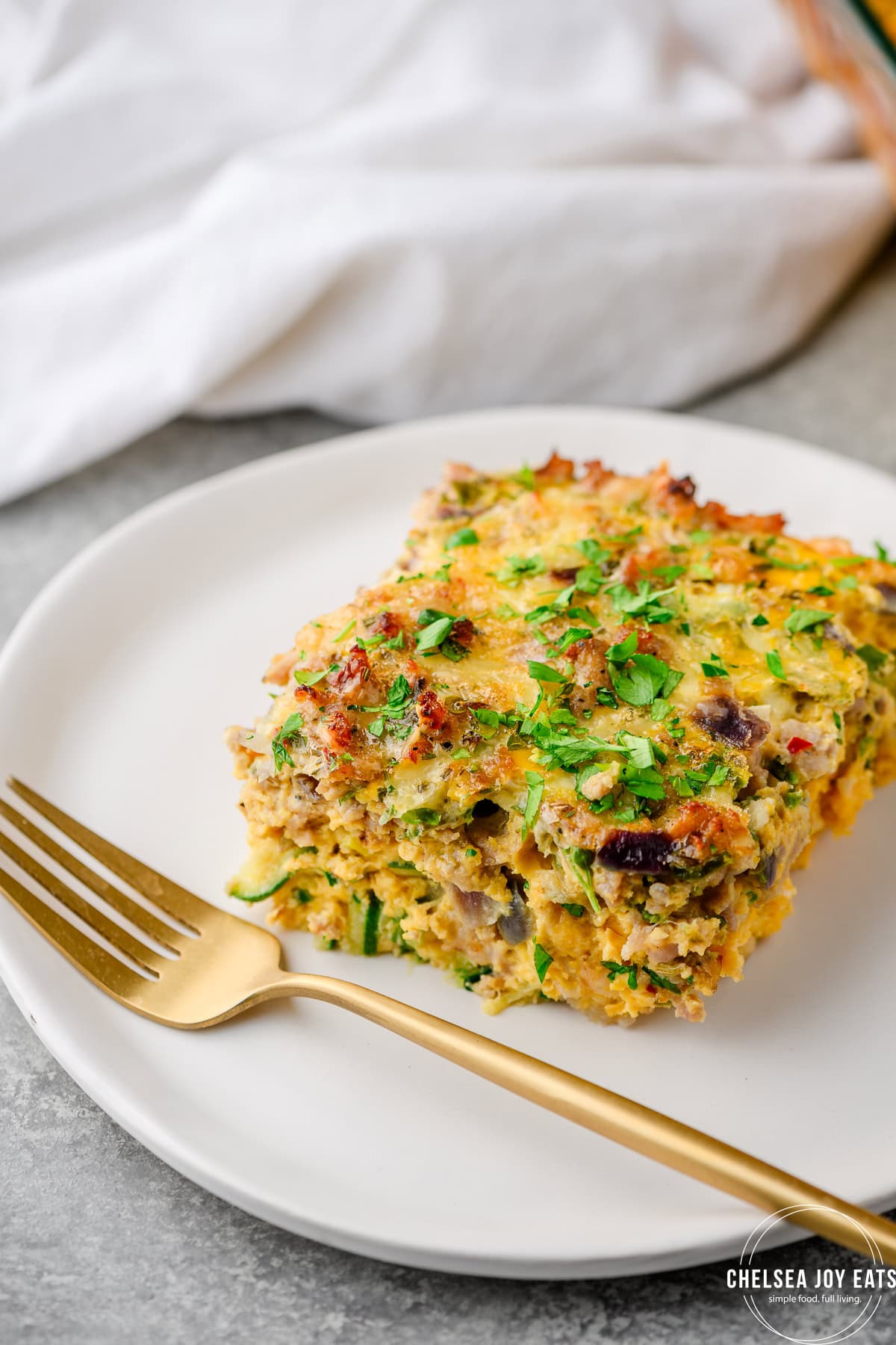 Closeup of a serving of zucchini sausage breakfast casserole on a white plate with a fork