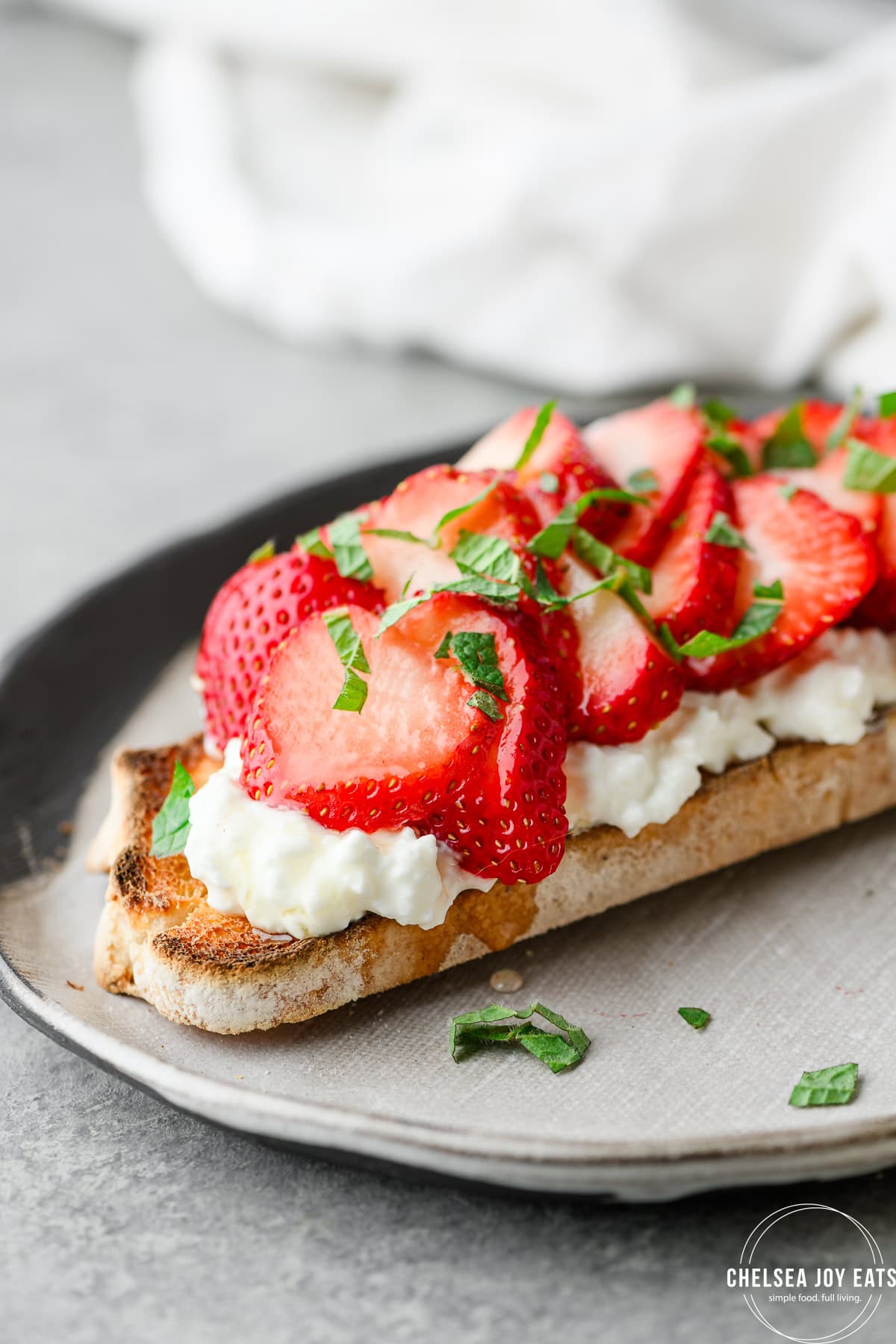Closeup of sourdough toast topped with cottage cheese, strawberries, honey, and mint