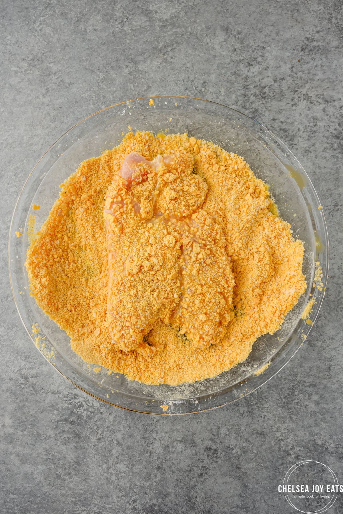 Chicken cutlet being breaded with cornflakes in a shallow pie dish