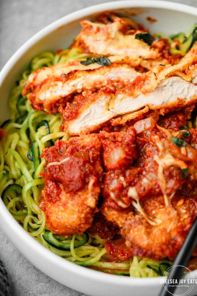 Closeup of sliced gluten free chicken parmesan served over zucchini noodles