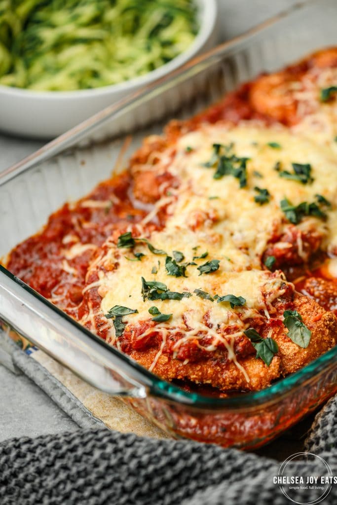 Casserole dish with gluten free chicken parmesan in marinara sauce and topped with cheese