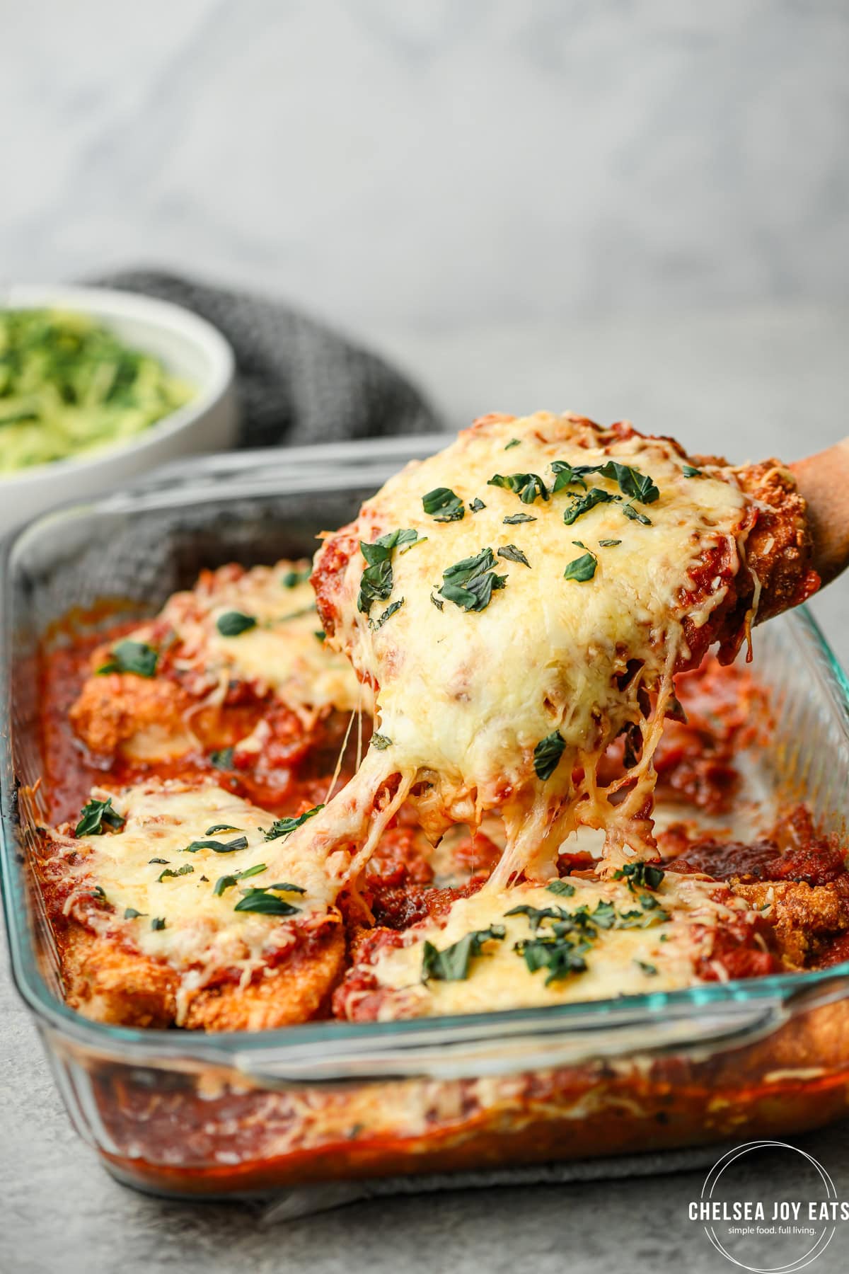 Gluten free chicken parmesan being lifted out of a casserole dish with stretching melty cheese