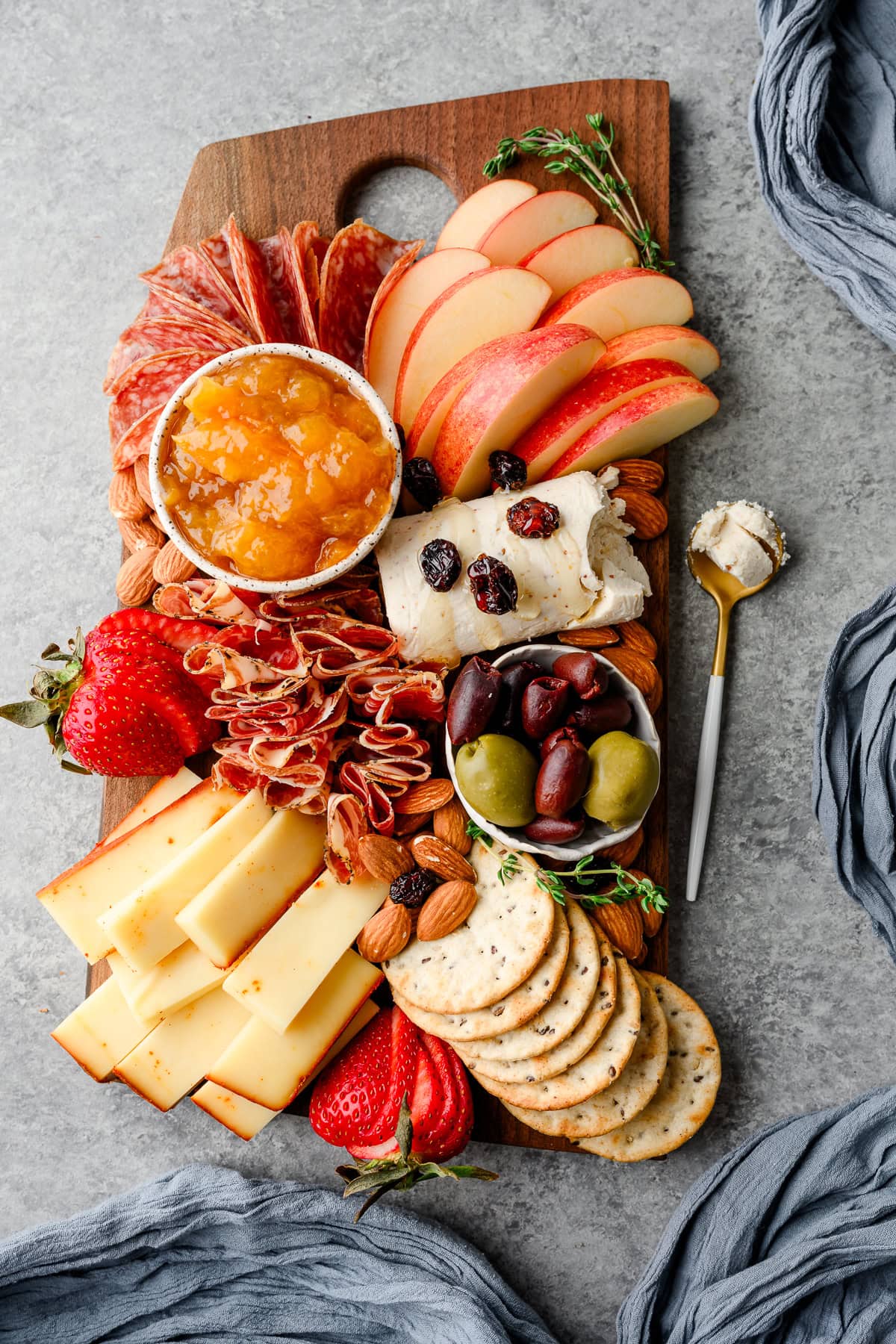 Small charcuterie board with salami, pepperoni, cheese, crackers, goat cheese, jam, olives, and apples