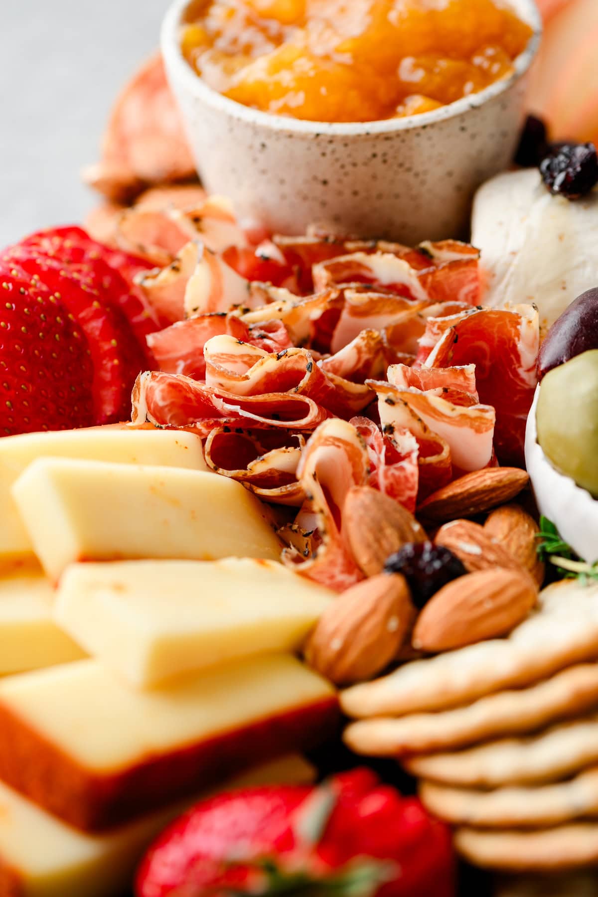 Closeup of proscuitto on a charcuterie board along with apricot jam, nuts, cheese, and crackers